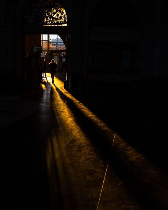 Silhouette of a person walking through a sunlit archway in a building, creating a dramatic lighting effect.