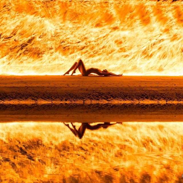 A nude woman is lying on a beach with water, reflecting the scene creating a sensual and dreamy atmosphere.