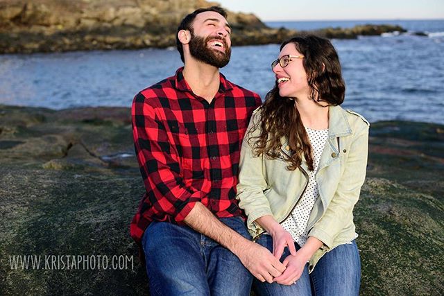 A happy couple laughs together by the sea, enjoying a loving moment outdoors. 
