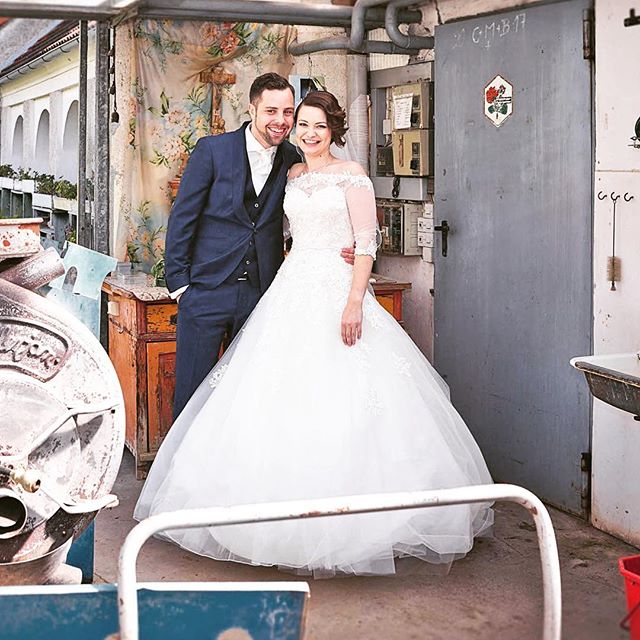 A happy couple in wedding attire pose indoors, radiating joy and celebrating their special day in a rustic setting.