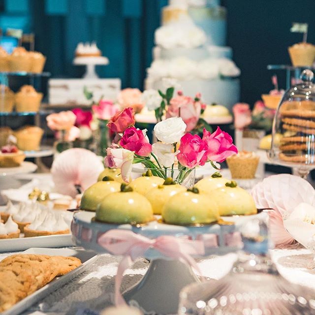 A dessert table displays an array of cakes, cupcakes, cookies, and flowers for a special event.