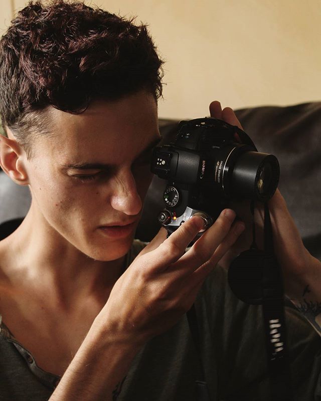A young man is focused on taking a picture with a Canon camera in an indoor setting.