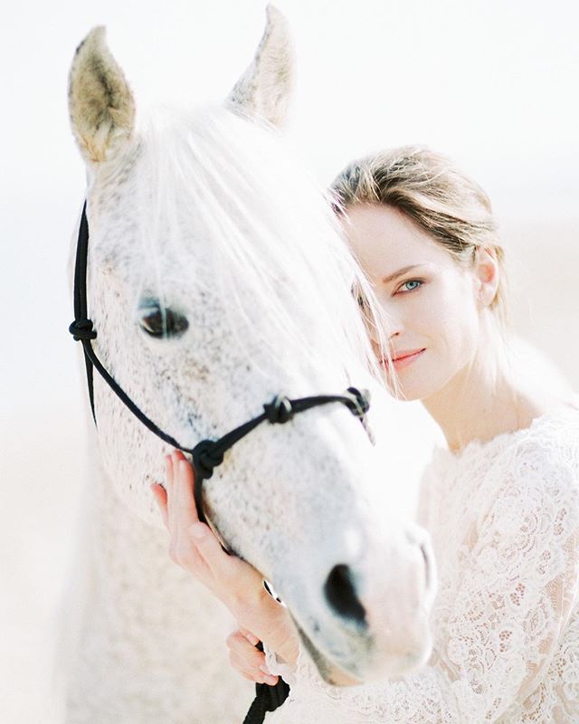 A woman gently embraces a white horse on a serene beach, creating a dreamlike scene.