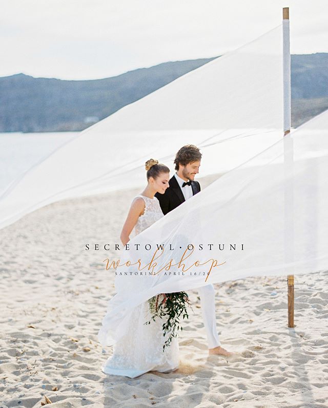 A bride and groom walk barefoot on a sandy beach under a white cloth, creating a romantic wedding moment.