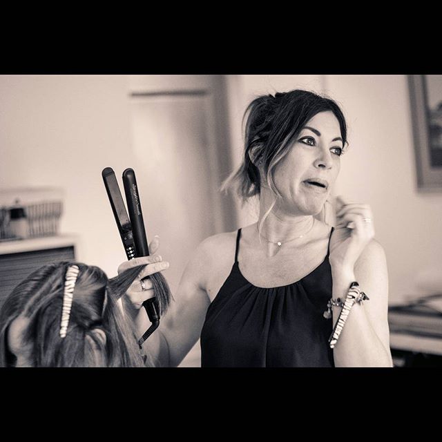 A hairdresser styles a client's hair using a hair straightener in a vintage-style indoor setting.