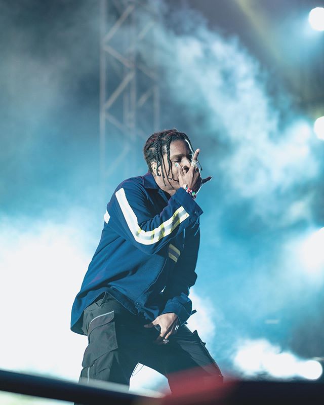 A$AP Rocky performs live on stage during a concert, under artificial lights and surrounded by smoke.