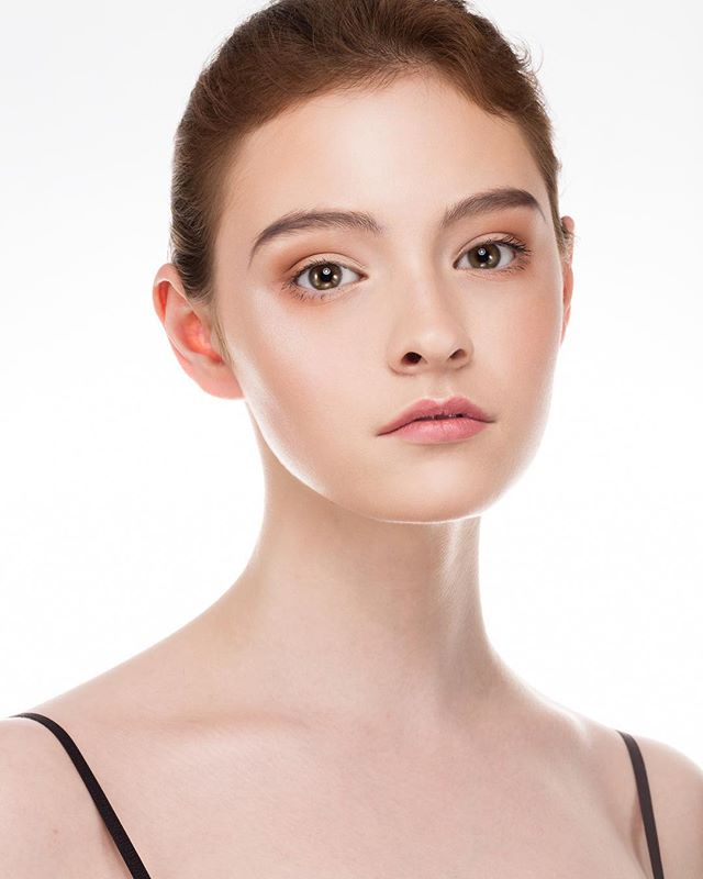 A young woman with fair skin poses against a white background, showcasing a minimalist and natural beauty look.