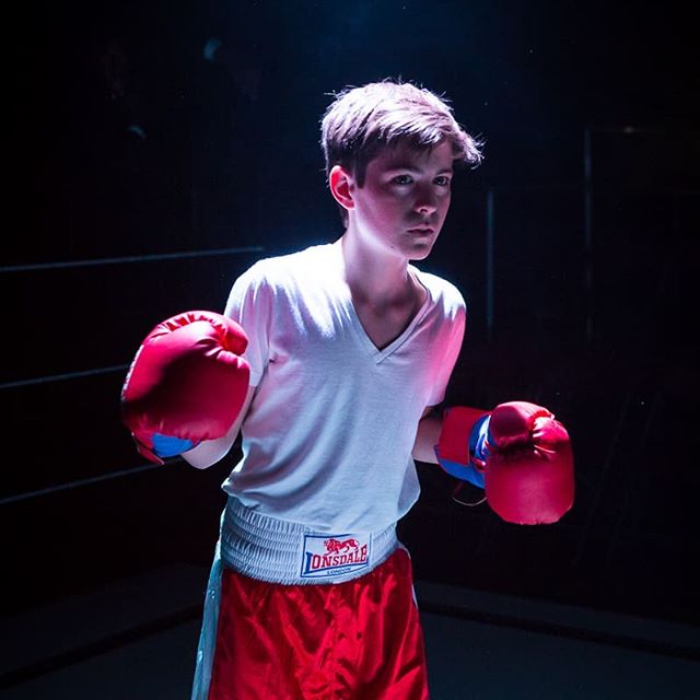 A determined teenage boxer stands in a boxing ring, ready for the fight.