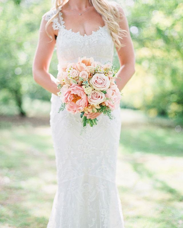 A bride holds a bouquet of pastel flowers in her wedding dress, outdoors on her special day.