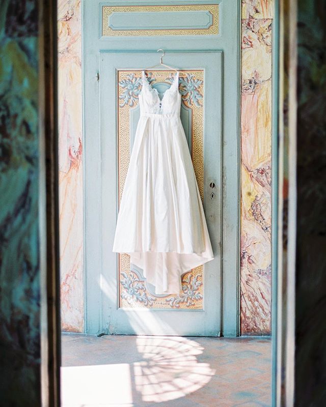 A white wedding dress hangs elegantly on a decorative blue door, bathed in soft, dreamy light.