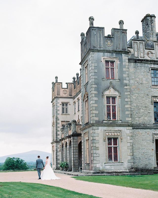 A bride and groom walk towards a stately castle on their wedding day, a romantic and elegant scene.