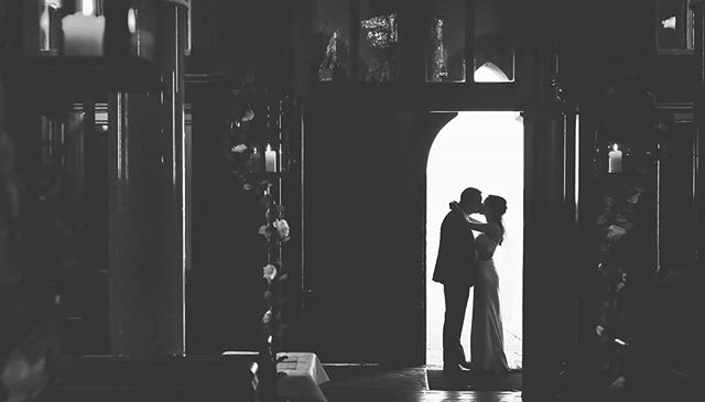 A bride and groom are silhouetted in a doorway, sharing a kiss in a church setting.