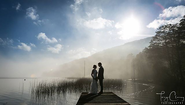 A bride and groom stand in silhouette on a pier against a misty lake backdrop, perfect for wedding or romantic getaway themes.