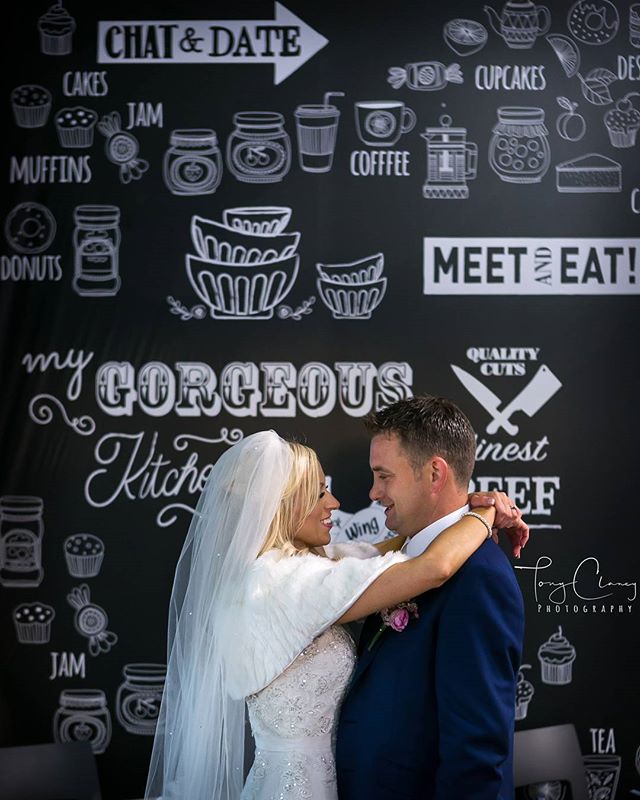 A bride and groom share an intimate moment during their wedding reception in front of a decorative wall.