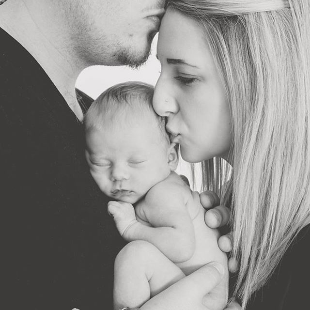 A tender black and white photo of a family, with mother and father kissing their newborn baby.
