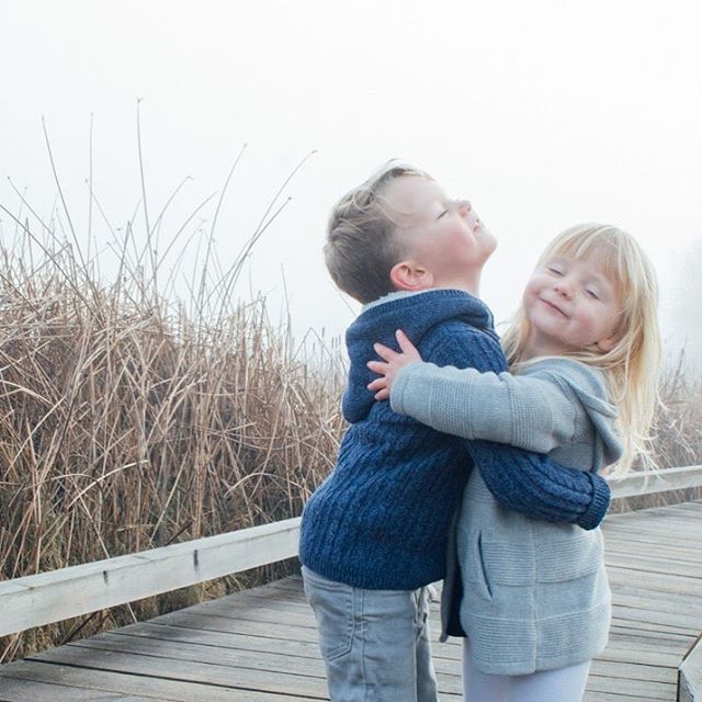Two young siblings share a loving embrace on a boardwalk in nature.