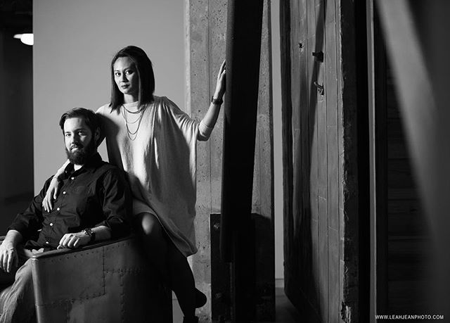 A stylish couple poses indoors in a black and white portrait, looking serious and intimate.