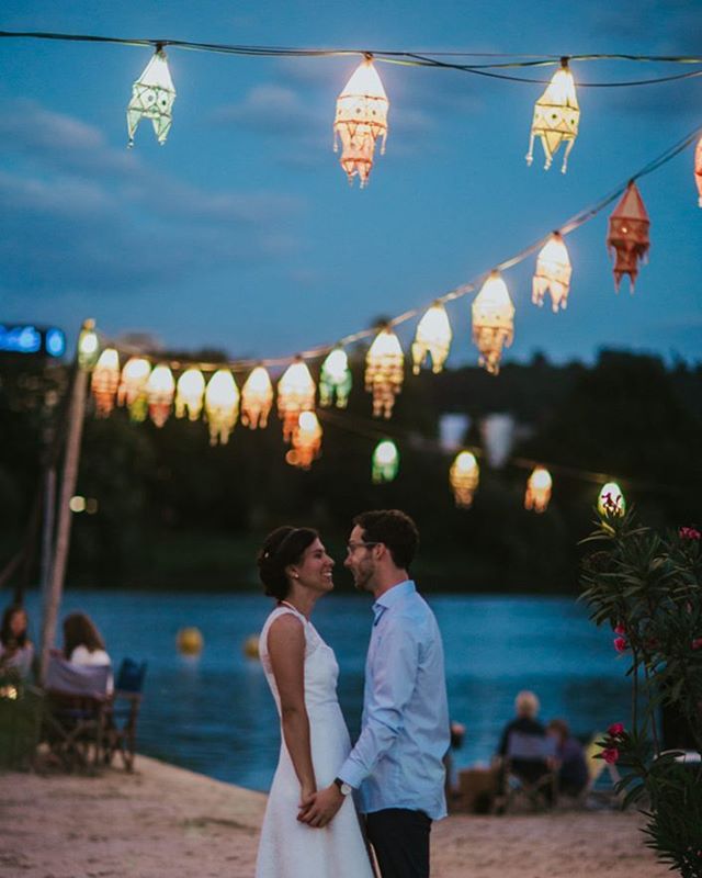 A bride and groom hold hands under string lights at their beach wedding reception at night.