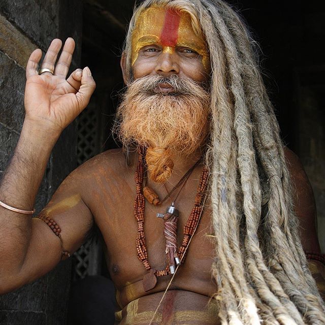 An Indian Sadhu is a holy man with dreadlocks, face paint, beard, and jewelry outside of a temple.