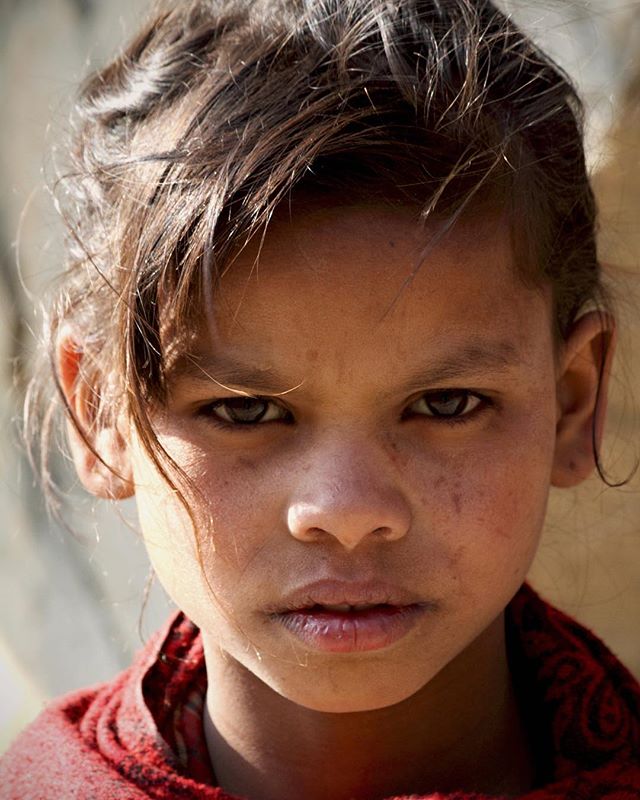 A portrait of a young girl with a serious expression looks directly at the camera in soft, natural light.