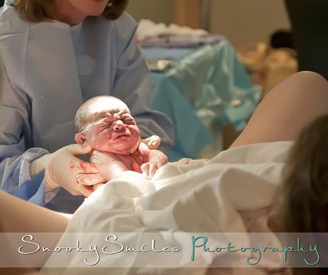 A newborn baby is held by a doctor in a delivery room after birth.