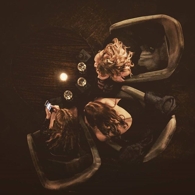 Three women are sitting around a table enjoying drinks in a dimly lit bar.