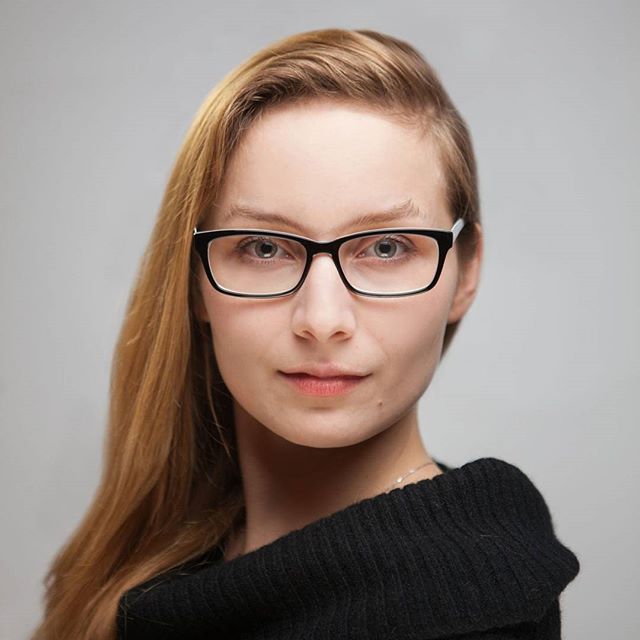 A woman with blonde hair and glasses poses for a professional headshot in a studio setting.
