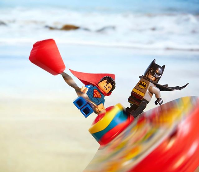 Lego Superman and Batman figurines on a colorful spinning top at the beach. 