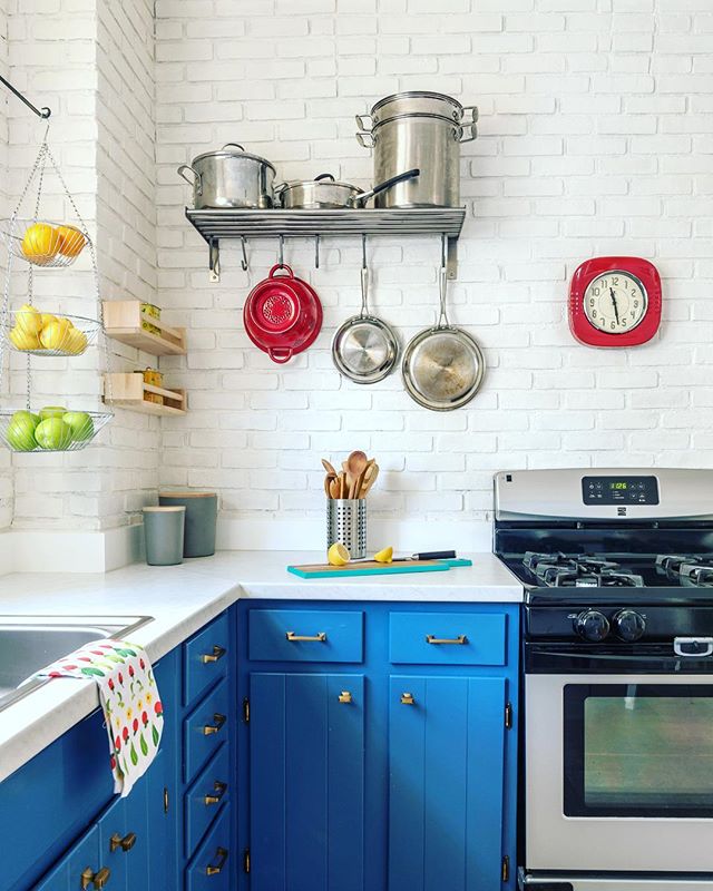 A bright kitchen features blue cabinets, stainless steel appliances, and colorful accessories.