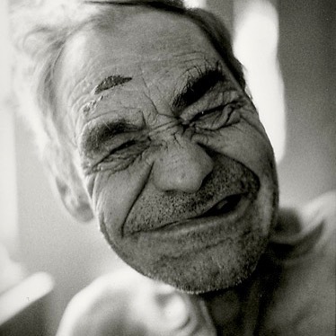 A black and white close-up portrait of an elderly man with an intense and emotional expression.