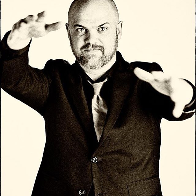 Portrait of a confident man in a suit with outstretched hands, in a sepia studio shot.