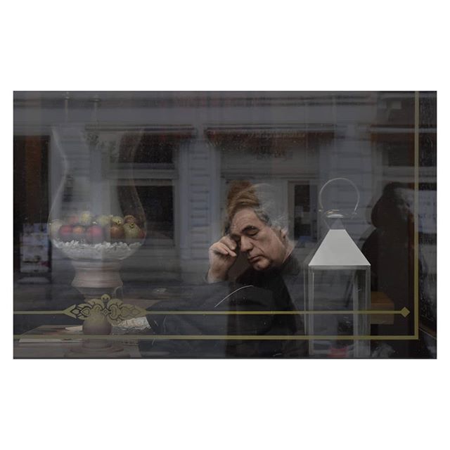 A man sits thoughtfully near a window, reflected images creating a layered, emotive scene.