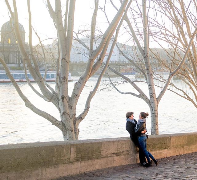 A couple embraces by the Seine River in Paris at sunset, creating a romantic travel moment.