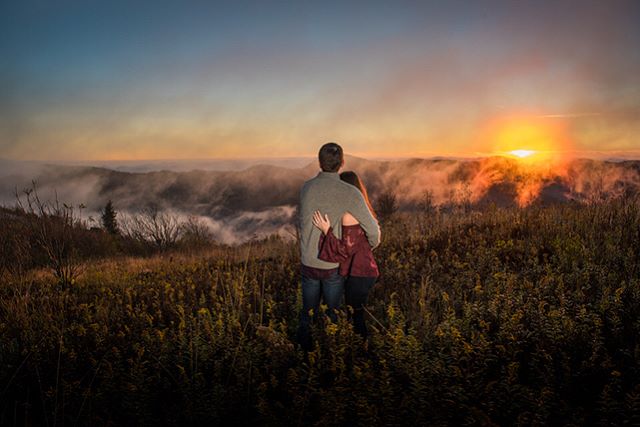A couple embraces, gazing at a vibrant sunset over misty mountains, symbolizing love and adventure.
