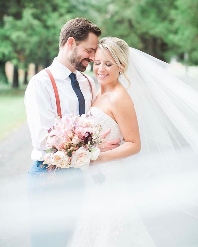 A bride and groom embrace tenderly on their wedding day, holding a bouquet with soft lighting.
