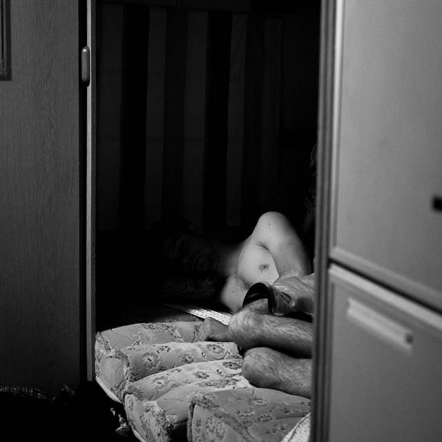 A shirtless man is lying on a floral mattress in a dimly lit room, captured in black and white.