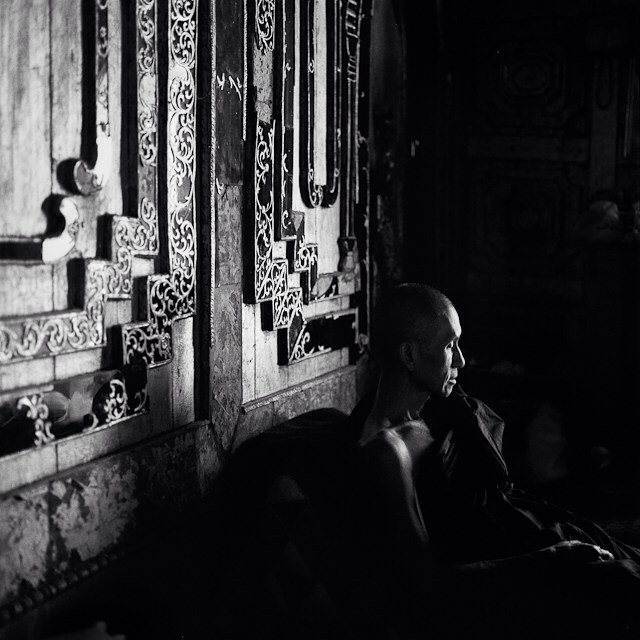 A contemplative monk sits in a temple, the monochrome image evokes serenity and introspection.