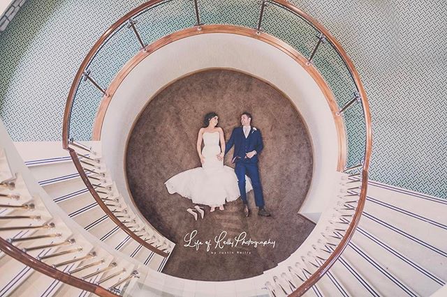A bride and groom lie on the floor inside a spiral staircase for a romantic wedding photo.