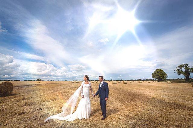 A bride and groom holding hands in a golden field with hay bales on their wedding day.