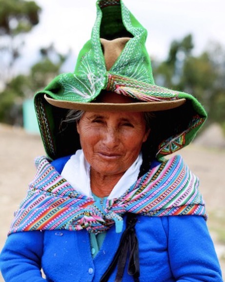 A woman in traditional Peruvian clothing and a distinctive hat smiles outdoors.