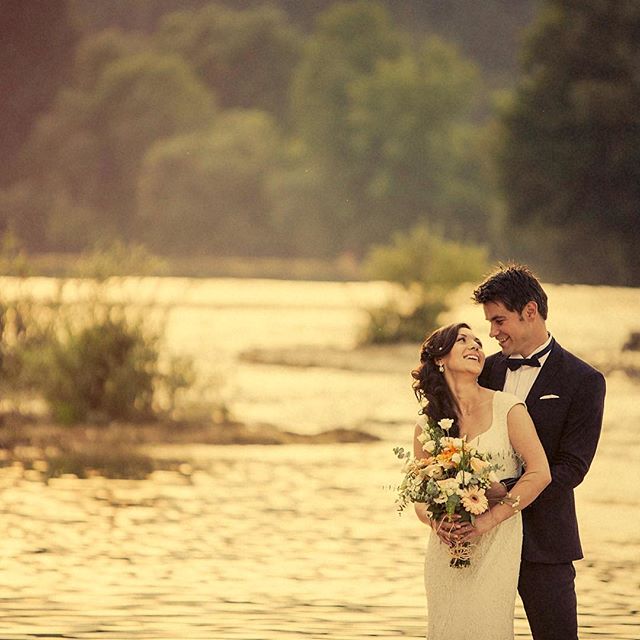 A bride and groom lovingly embrace by a river at their wedding.