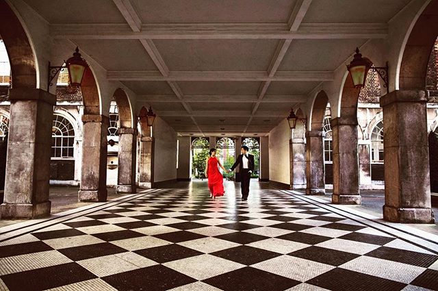 A couple holds hands walking through an elegant arcade with a black and white tiled floor.