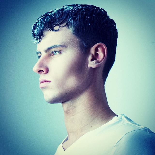 A male model is captured in a profile shot with cool lighting and a contemplative mood, ideal for editorial or social media use.