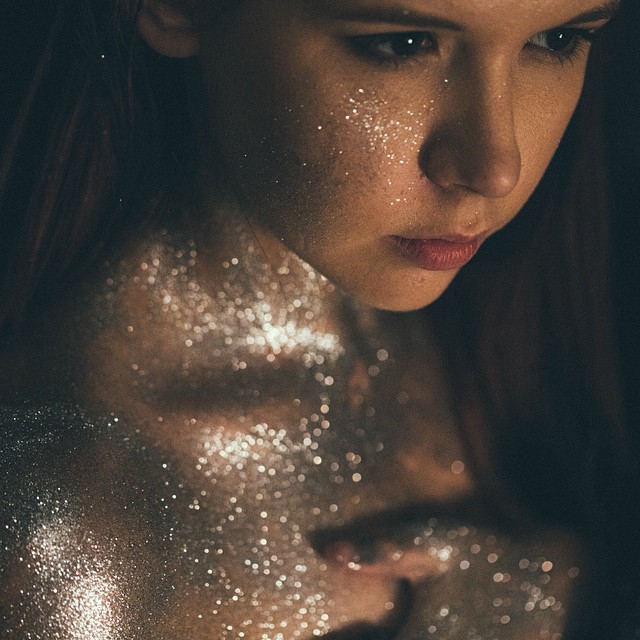 A woman's face and chest are covered in shimmering glitter, creating an ethereal and captivating close-up.