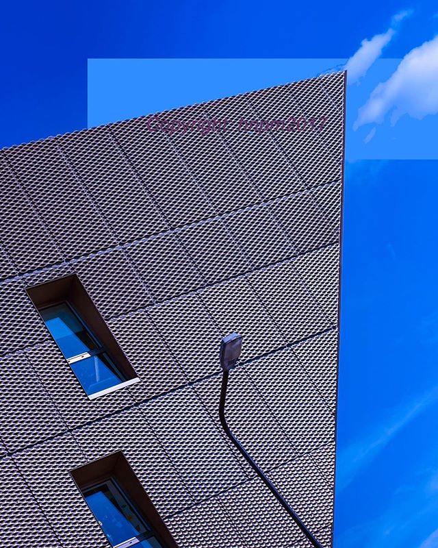 An architectural shot of a modern building with an interesting facade and windows against a bright blue sky.