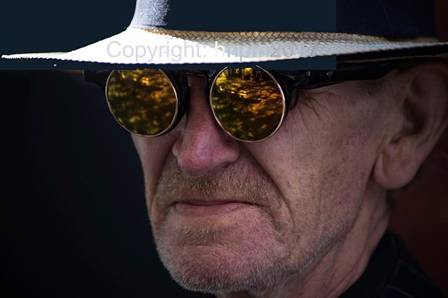 Close up of a stylish senior man with glasses and hat, captured in soft, warm lighting.