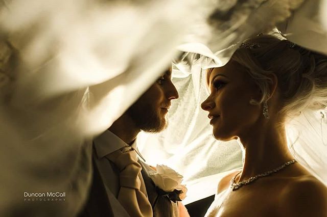 A bride and groom share an intimate moment under a veil on their wedding day.