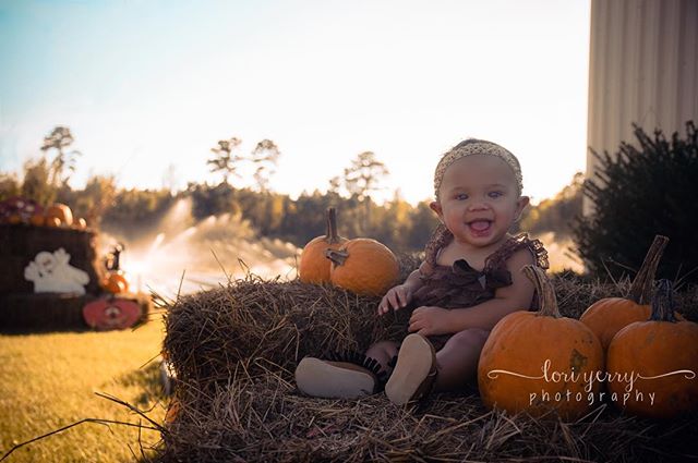 A happy baby sits amongst pumpkins on a hay bale, enjoying an autumn day.