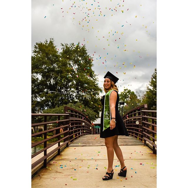 A graduate celebrates her achievement with confetti on a bridge in an outdoor setting. 