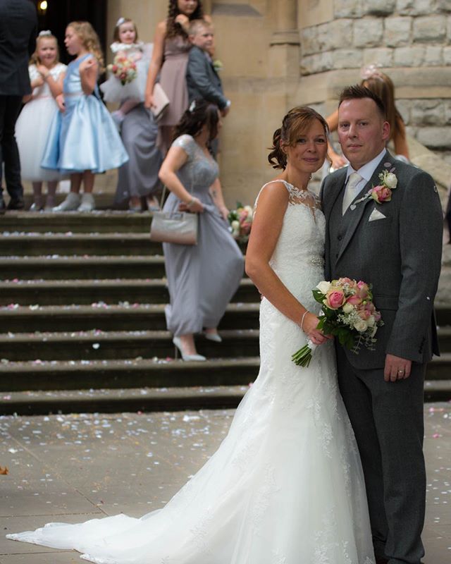 A newlywed couple poses with their wedding party on steps outside a building.